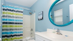 A bathroom with a striped shower curtain, a toilet, a sink with a mirror, and a framed sign on the wall. - Townhome 2 blocks from beach. Sleeps 10! (Carolina Beach)