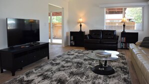 Una sala de estar moderna con televisor de pantalla plana, sofá de cuero negro y una mesa de centro de vidrio.