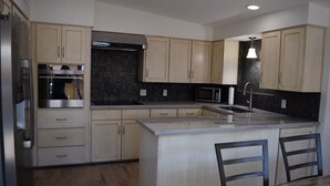 Una cocina moderna con armarios de madera clara, una isla central con taburetes de bar, horno integrado y microondas.