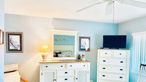 Une chambre à coucher comprenant un lit, une commode, une chaise, un téléviseur et un ventilateur de plafond.