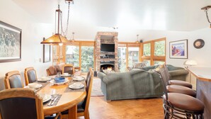A spacious living area with a fireplace, wooden furniture, and large windows offering a view of the outdoors. - Across from Lift 7 | 2BR + Loft | Hot Tubs, Fireplace, Walk to Town (Telluride)