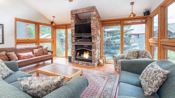 A spacious living room with a stone fireplace, large windows, and comfortable seating. - Across from Lift 7 | 2BR + Loft | Hot Tubs, Fireplace, Walk to Town (Telluride)