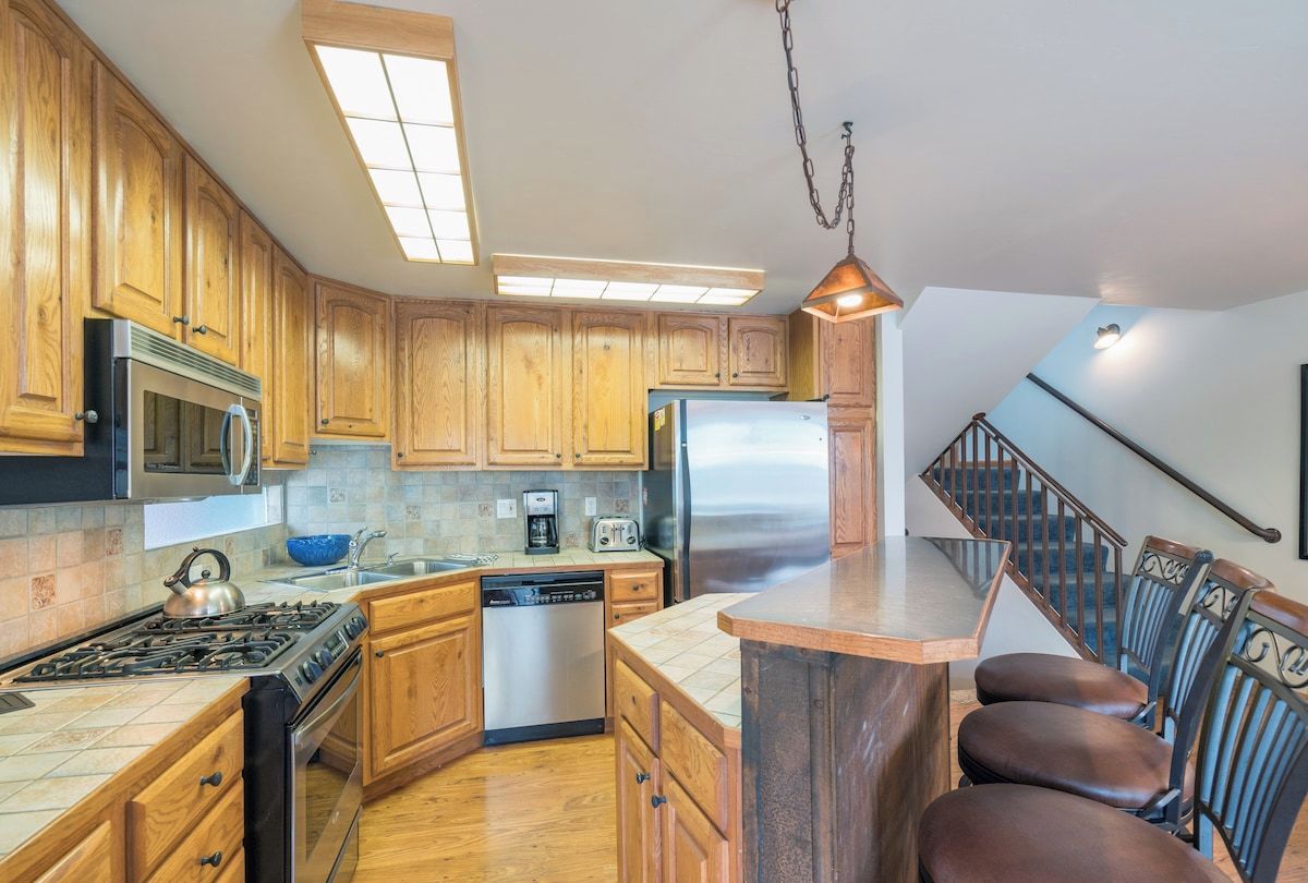 A kitchen with wooden cabinets, stainless steel appliances, a dishwasher, and a bar area with chairs.