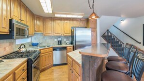 A kitchen with wooden cabinets, stainless steel appliances, a dishwasher, and a bar area with chairs. - Telluride Lodge Condo 411 (Telluride)