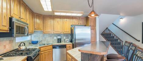 A kitchen with wooden cabinets, stainless steel appliances, a dishwasher, and a bar area with chairs.