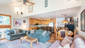 A spacious living room with a large sofa, a coffee table, and a dining area with a table and chairs. The kitchen is visible in the background with wooden cabinets and modern appliances. - Across from Lift 7 | 2BR + Loft | Hot Tubs, Fireplace, Walk to Town (Telluride)