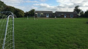 A grassy field with a soccer goal, a building with a door and windows, and a clear sky. - Visit Wales 4 Star, rural bungalow - Sauna, jacuzzi, play area and Free Wi-fi  (Pontypool near Usk, Panteg)