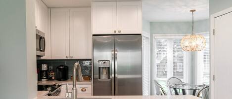 A modern kitchen with white cabinets, stainless steel appliances, a water dispenser, and a pendant light.