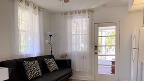 Uma sala de estar com um sofá preto, almofadas estampadas, um abajur e uma porta que dá para o exterior.