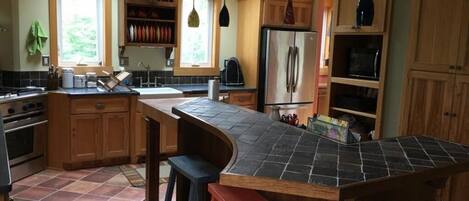 Eine Küche mit Kochinsel, Holzschränken, einem Edelstahlkühlschrank und einem Fenster für natürliches Licht.