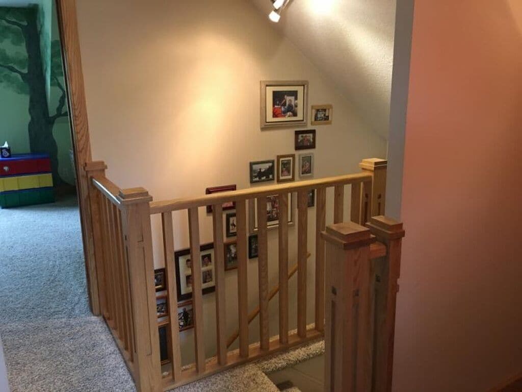 A wooden staircase with a railing, carpeted steps, and framed pictures on the wall.