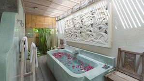 A bathroom with a freestanding bathtub filled with rose petals, a wooden bench, and a decorative wall panel.