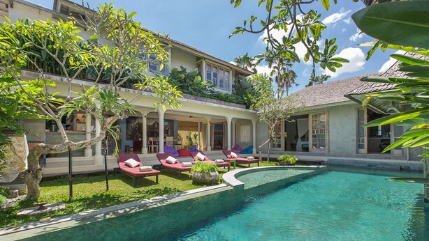 A pool area with lounge chairs and a building with a tiled roof.