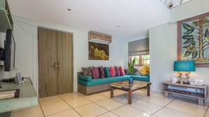 A modern living room with a teal sofa, colorful cushions, a coffee table, and a painting on the wall.