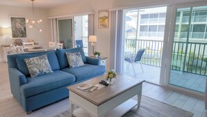 En moderne stue med blå sofa, sofabord og balkon med hav- og byudsigt.