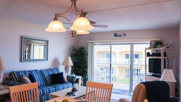 A living room with a sofa, chairs, a dining table with fruit, a lamp, and a ceiling fan.