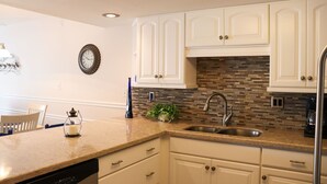 A kitchen with white cabinets, a tiled backsplash, a stainless steel sink, and a clock on the wall.