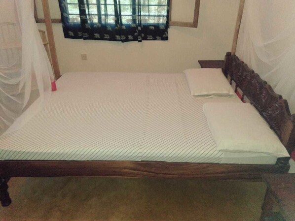 Una cama individual con estructura de madera y ropa de cama blanca, una ventana con cortina estampada y una pared blanca.