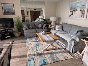 A living room with a sofa set, a coffee table, a TV, and a plant. - House Of The Sun #212GV (Sarasota)