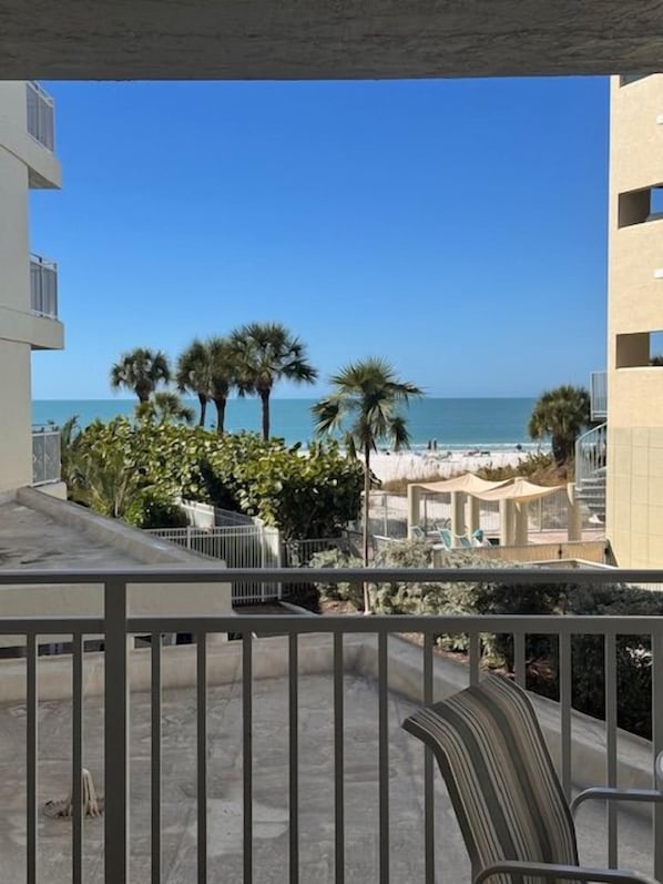 A balcony with a view of the beach and ocean, a chair, and a railing.