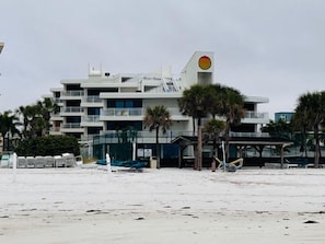 A beachfront hotel with multiple balconies, palm trees, and a sandy beach.
