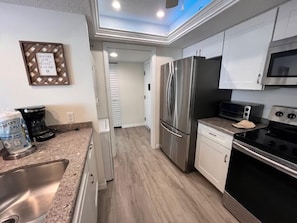 A modern kitchen with stainless steel appliances, a granite countertop, and a wooden floor.