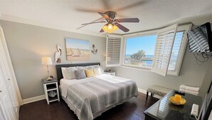 Ein Schlafzimmer mit einem Bett, Nachttischen, einem Deckenventilator, Kunstwerken und einem Fenster mit Blick.