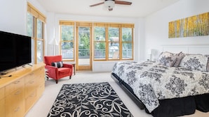 A bedroom with a bed, a TV, a red chair, a ceiling fan, and large windows. - Willow 302 2 Bedroom/2 1/2 Bath Condo (Telluride)