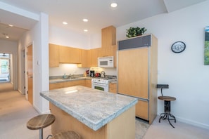 A modern kitchen with granite countertops, wooden cabinets, a built-in microwave, and a stainless steel refrigerator.