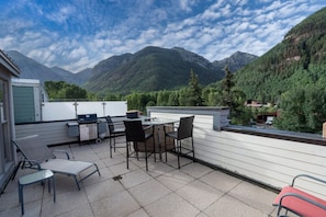 Une terrasse avec une table et des chaises, un barbecue et une vue sur les montagnes.