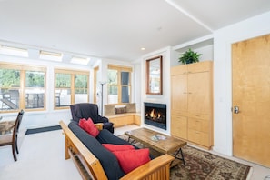 A modern living room with a fireplace, wooden furniture, and large windows.