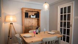 A dining area with a wooden table, chairs, a lamp, a wine bottle, and a glass on the table.