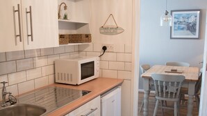 A compact kitchen with white cabinets, a microwave, a sink, and a dishwasher. There is a dining area with a table and chairs visible through an open doorway.