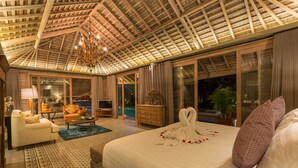 Ein geräumiges Schlafzimmer mit einem großen Bett, einer Chandelierleuchtre und Blick auf einen Swimmingpool.