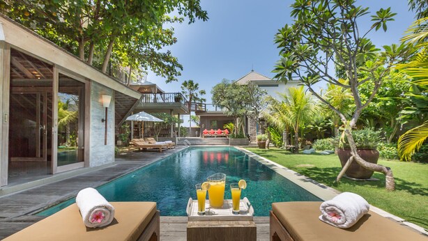 Ein Poolbereich mit Liegestühlen, einem Holztisch mit Getränken und Blick auf ein Haus und einen Garten.