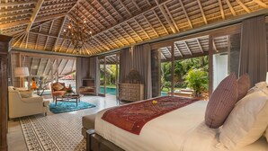 Ein geräumiges Schlafzimmer mit einem großen Bett, einer Sitzecke inklusive Sofa und Sessel, einem Couchtisch und Blick auf einen Pool und Grünflächen.