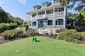 A two-story house with a porch, outdoor seating, and a green lawn.