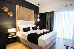 Et moderne hotelværelse med en stor seng, et natbord med lampe, en vægmonteret klimaanlæg og udsigt til det frie gennem lette gardiner.