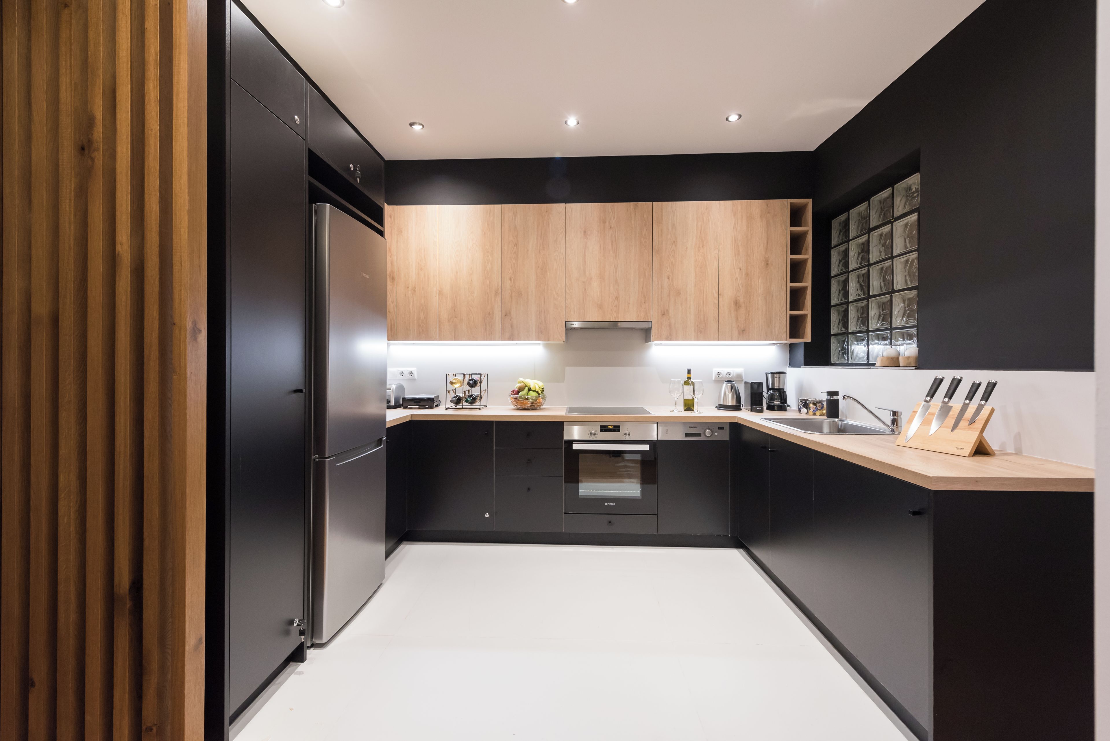 A modern kitchen with black cabinets, a stainless steel refrigerator, a built-in oven, and a wooden countertop.