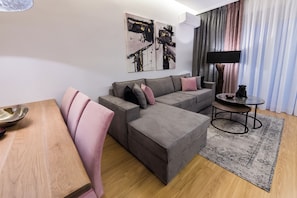 Een moderne woonkamer met een hoekbank, een klein rond tafeltje en een flatscreen televisie.