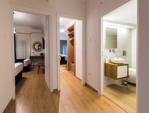 Une chambre d’hôtel avec un plancher en bois, un lit, un bureau avec une chaise, une armoire et une salle de bain avec un lavabo et un miroir.