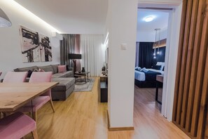 A modern living room with a sofa, a dining table, and a kitchen area in the background. - Acropolis Panoramic View Deluxe Apartment | 3 Falirou str 11742 Athens (Athina)