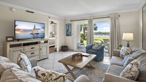 A living room with a TV, sofa, and a view of the outdoors. - 🌴 Welcome to The Islander #103 – Your Ultimate Destin Beach Escape! 🌅 (Destin)