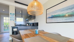 Uma cozinha moderna com uma mesa e cadeiras de madeira, um lustre pendente e um quadro de uma onda do mar na parede.