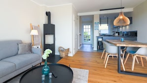 Uma sala de estar moderna com um sofá, mesa de centro e lareira. Uma cozinha com área de jantar visível ao fundo.