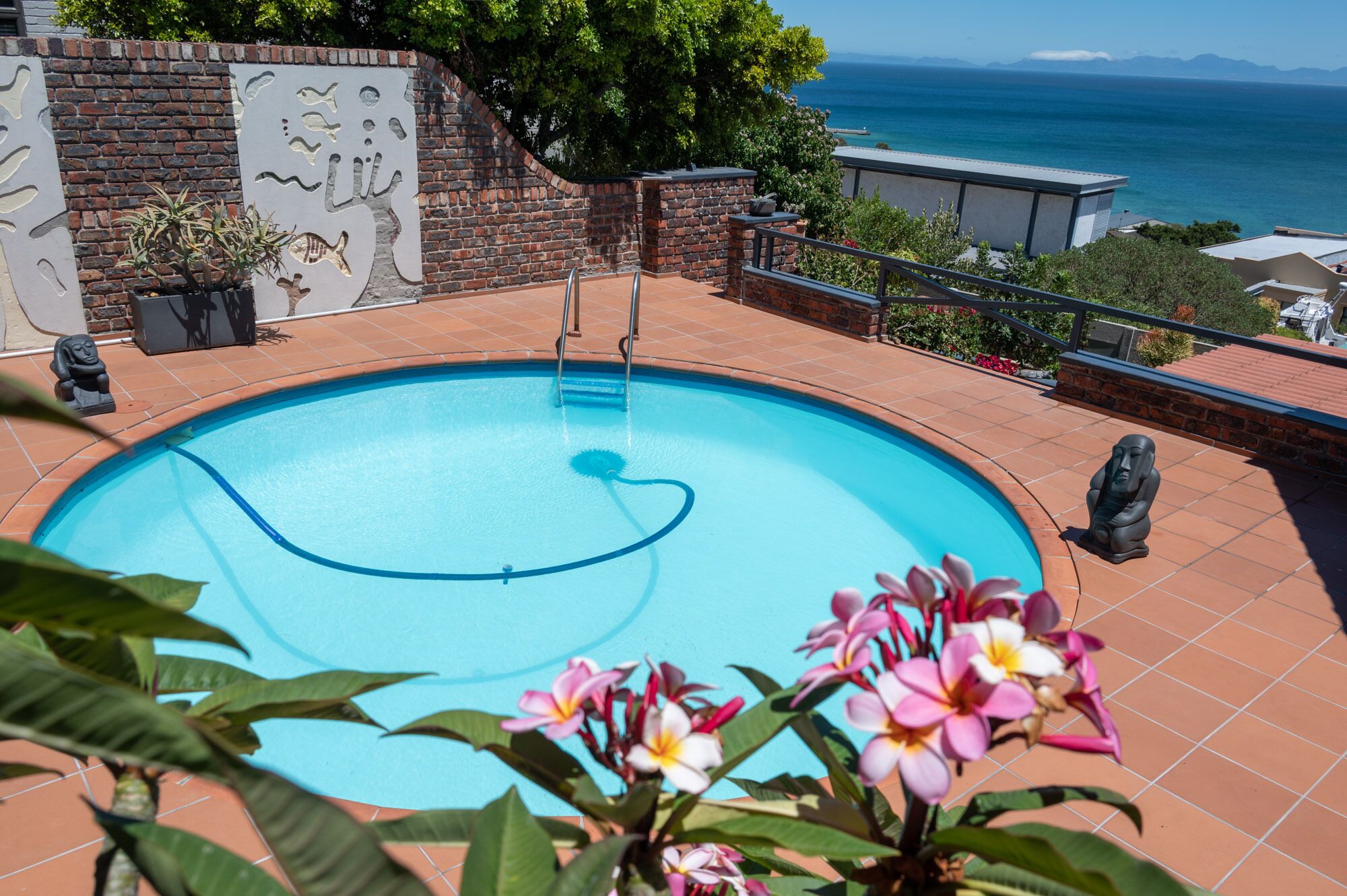 Une piscine avec vue sur la mer, entourée d’un mur de briques et agrémentée de plantes en pot.