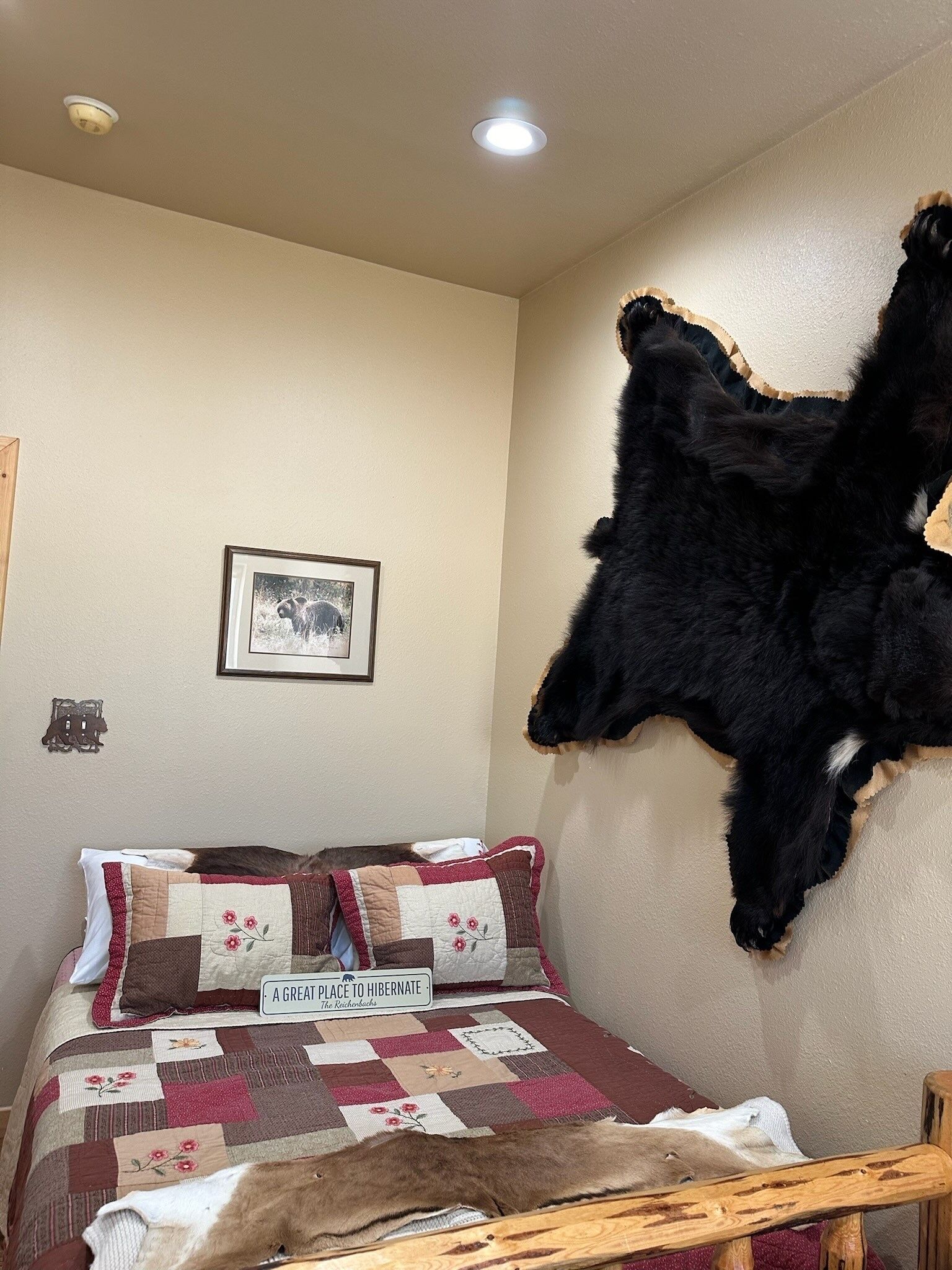 Une chambre à coucher avec un lit, une courtepointe, une peau d’animal empaillée accrochée au mur, un tableau encadré et une affiche sur le mur.