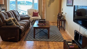 A cozy living room with a brown leather couch, a wooden coffee table, a mounted deer head, and a ceiling fan. - Welcome to our Mountain Lake Getaway (White Sulphur Springs)