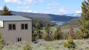 A single-story building with a metal roof, surrounded by a natural landscape with trees and a distant lake. - Welcome to our Mountain Lake Getaway (White Sulphur Springs)