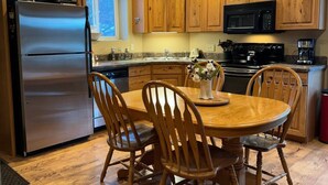 A kitchen with wooden cabinets, a stainless steel refrigerator, a microwave, a stove, and a dining table with chairs. - Welcome to our Mountain Lake Getaway (White Sulphur Springs)